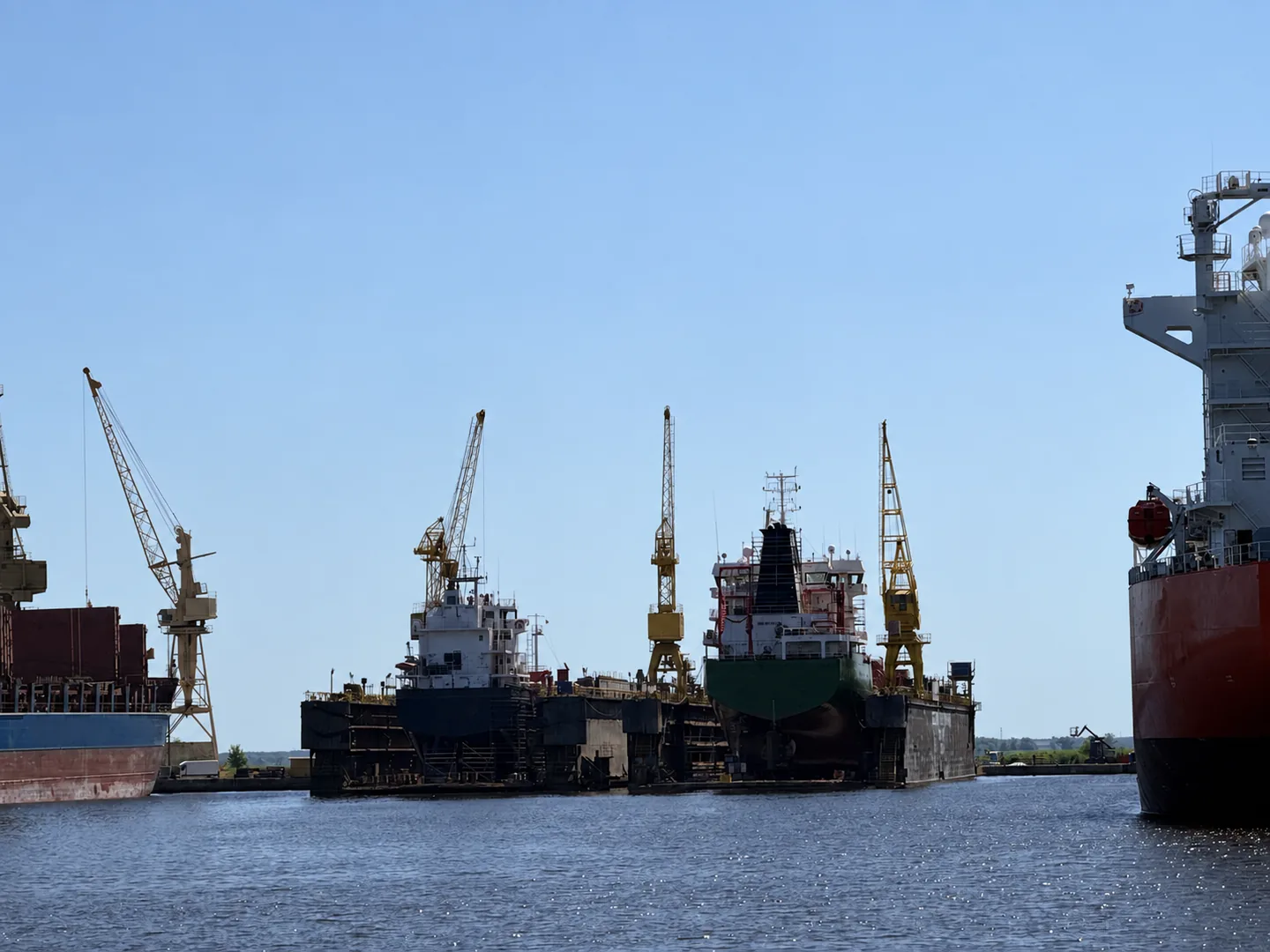 Commercial vessels alongside shipyard docks and cranes