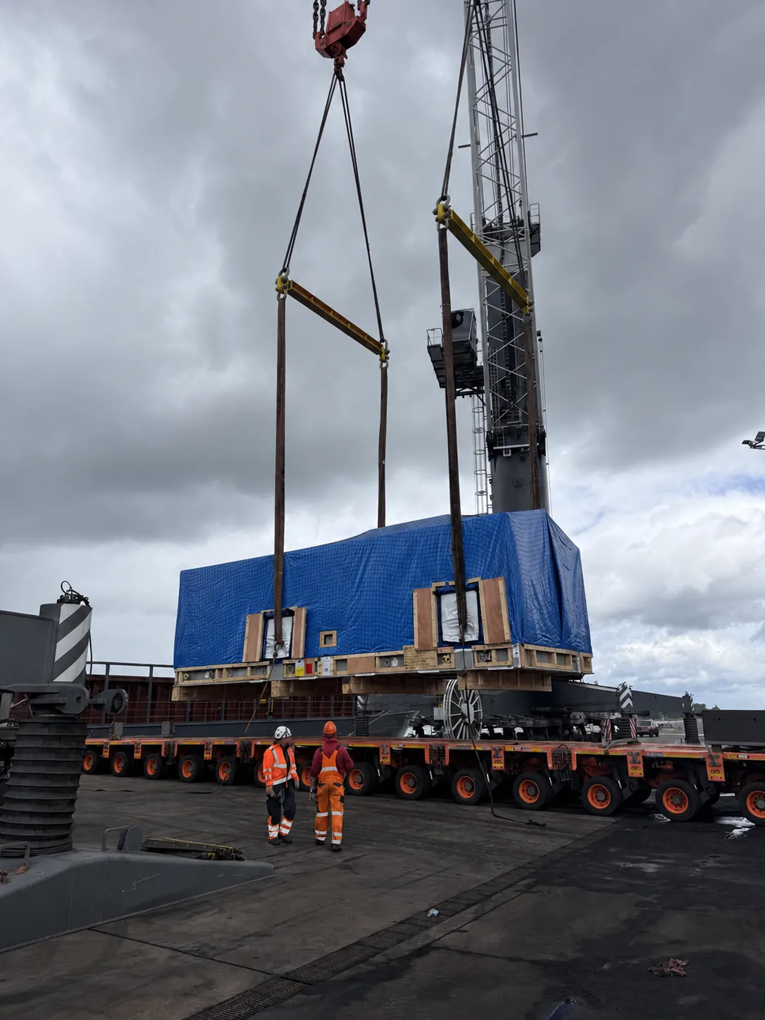 Heavy industrial module being lifted between a multi-axle transporter and vessel crane